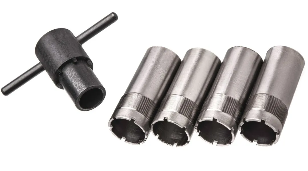 Four stainless-steel shotgun choke tubes beside a choke wrench