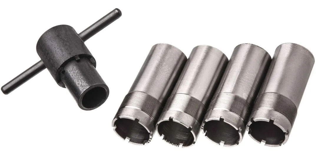 Four stainless-steel shotgun choke tubes beside a choke wrench