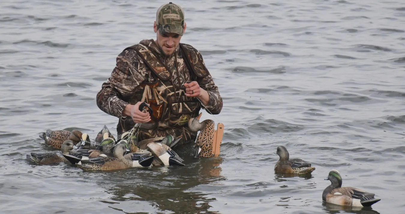 Hunter in camouflage standing in open water, setting out duck decoys