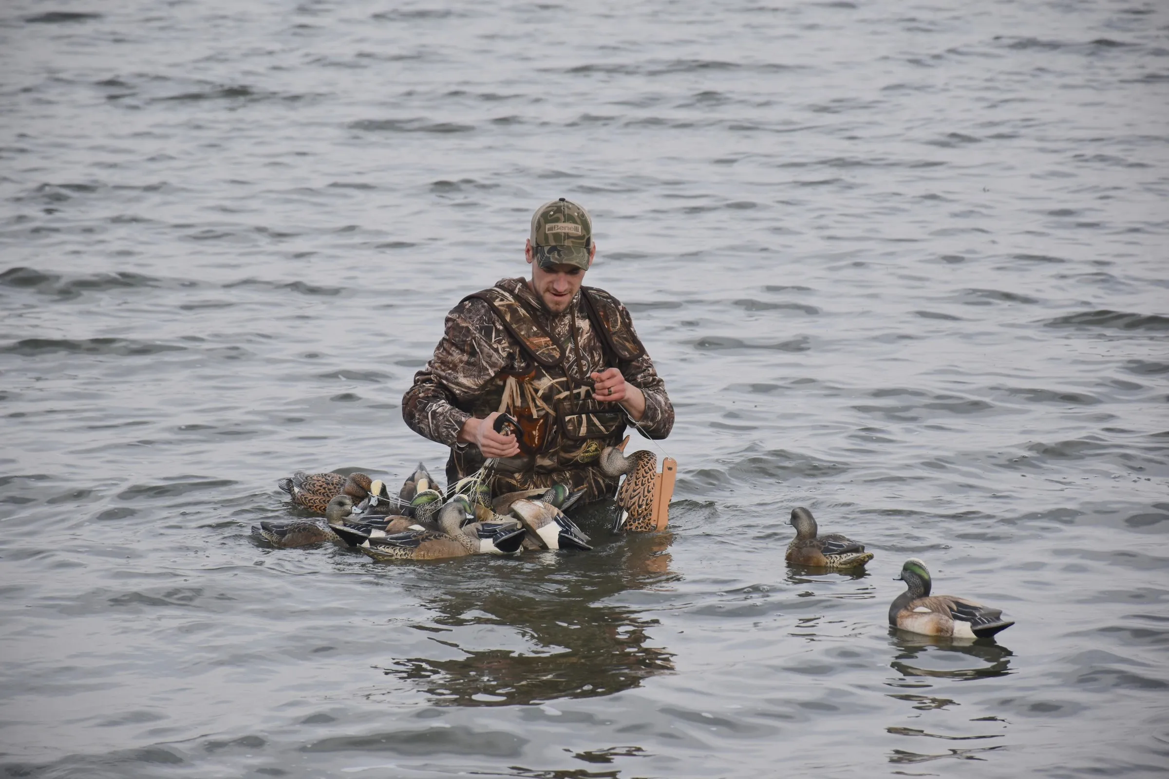 Hunter in camouflage standing in open water, setting out duck decoys